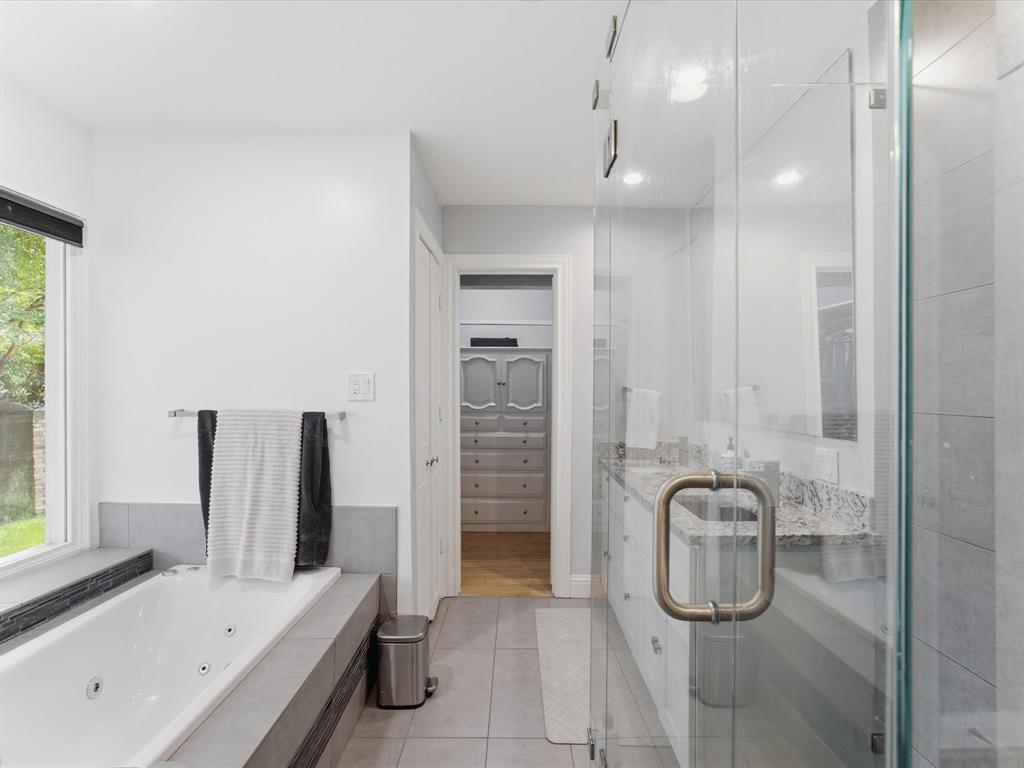 6160 Spring Valley Road Dallas, TX 75240 - Photo 27 of 40 Contemporary bathroom featuring a glass-enclosed shower with tile surround, a built-in jetted tub with tile surround, a dual vanity with granite countertop, and tile flooring