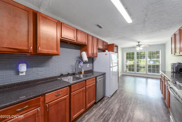 a kitchen with granite countertop wooden floors wooden cabinets and stainless steel appliances