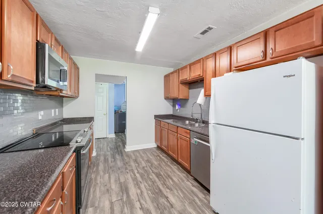 a kitchen with stainless steel appliances granite countertop a refrigerator a stove a sink dishwasher and wooden cabinets with wooden floor