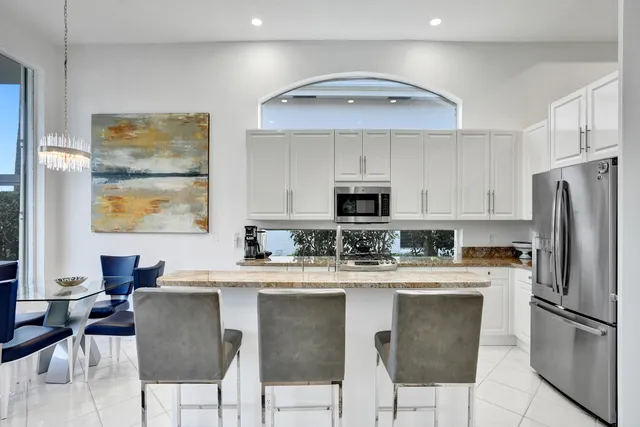 a kitchen with stainless steel appliances granite countertop a dining table chairs refrigerator and sink