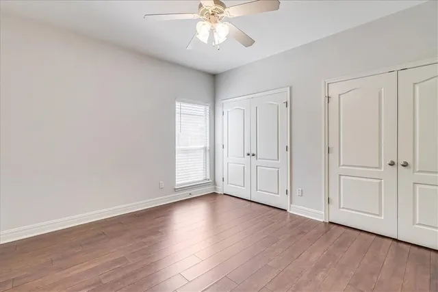 a view of an empty room with wooden floor and a ceiling fan