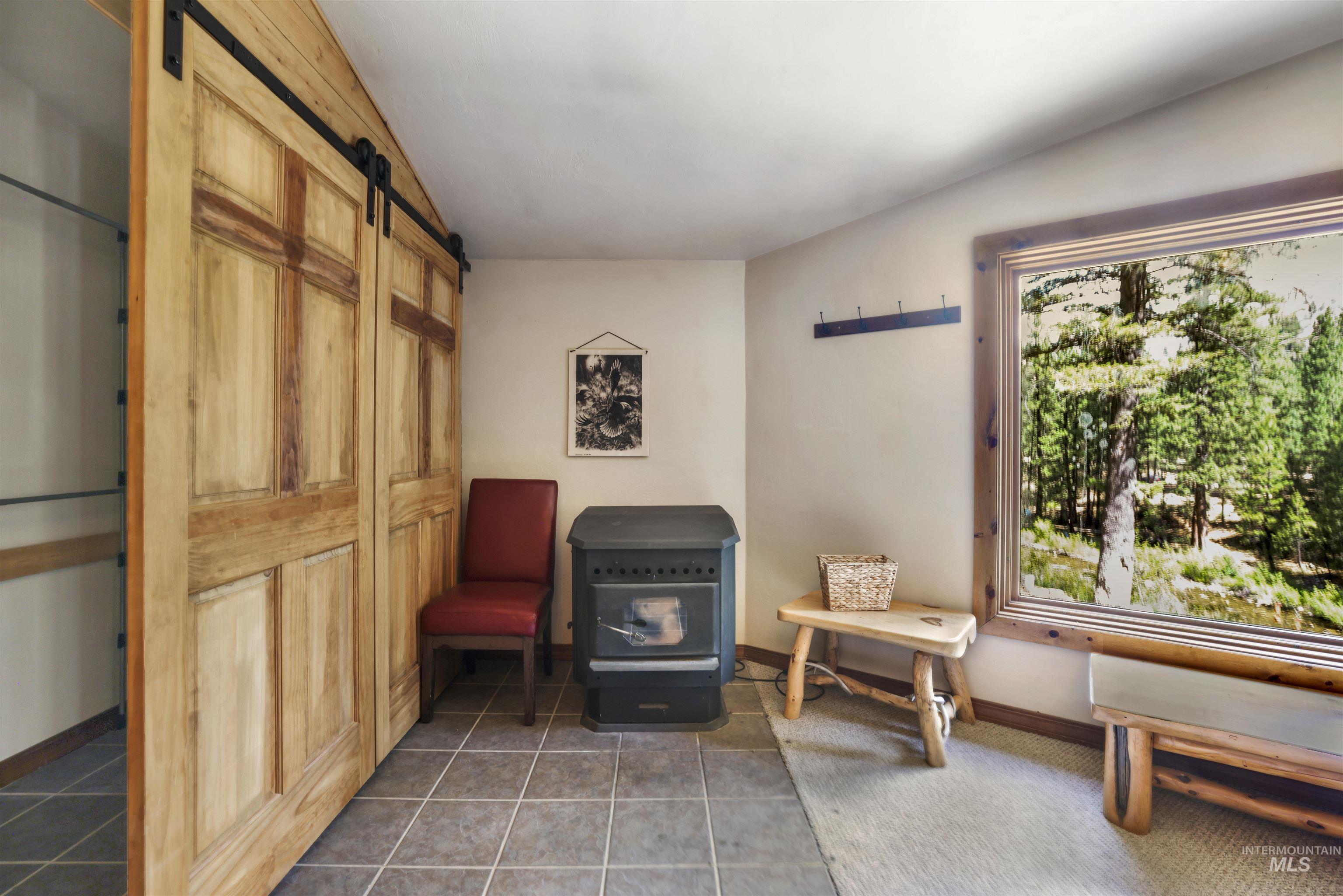 224 Dakota Road Mountain Home, ID 83647 - Photo 19 of 50 Wood-paneled sliding barn doors with exposed hardware, a built-in wood-frame window, a black freestanding stove, and tile flooring