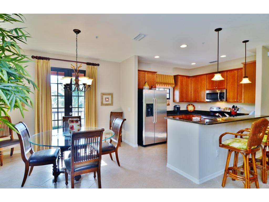 8997 Cambria Circle, Unit 2002 Naples, FL 34113 - Photo 7 of 18 a kitchen with stainless steel appliances kitchen island granite countertop a refrigerator a stove a kitchen island a dining table and chairs with wooden floor