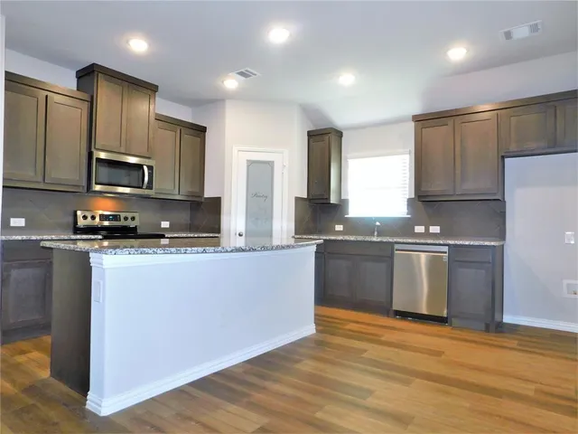 a large kitchen with stainless steel appliances granite countertop a stove a sink and a microwave