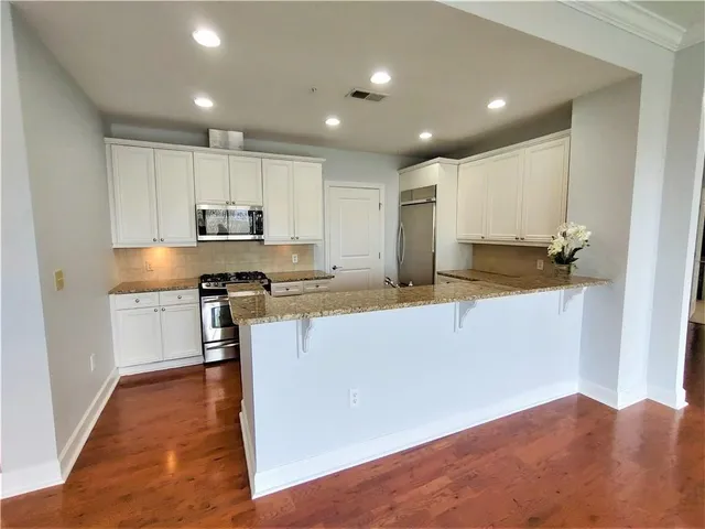 a kitchen with kitchen island granite countertop a stove a sink a refrigerator and white cabinets with wooden floor