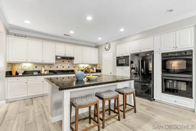 a kitchen with stainless steel appliances granite countertop a stove top oven a sink dishwasher a dining table and chairs with wooden floor