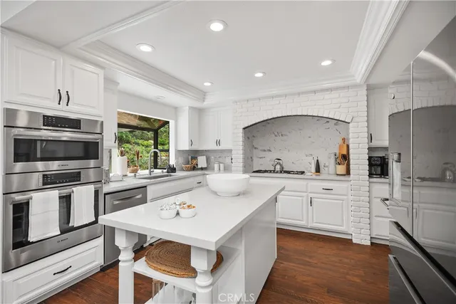 a kitchen with stainless steel appliances a stove a sink a microwave a refrigerator and white cabinets