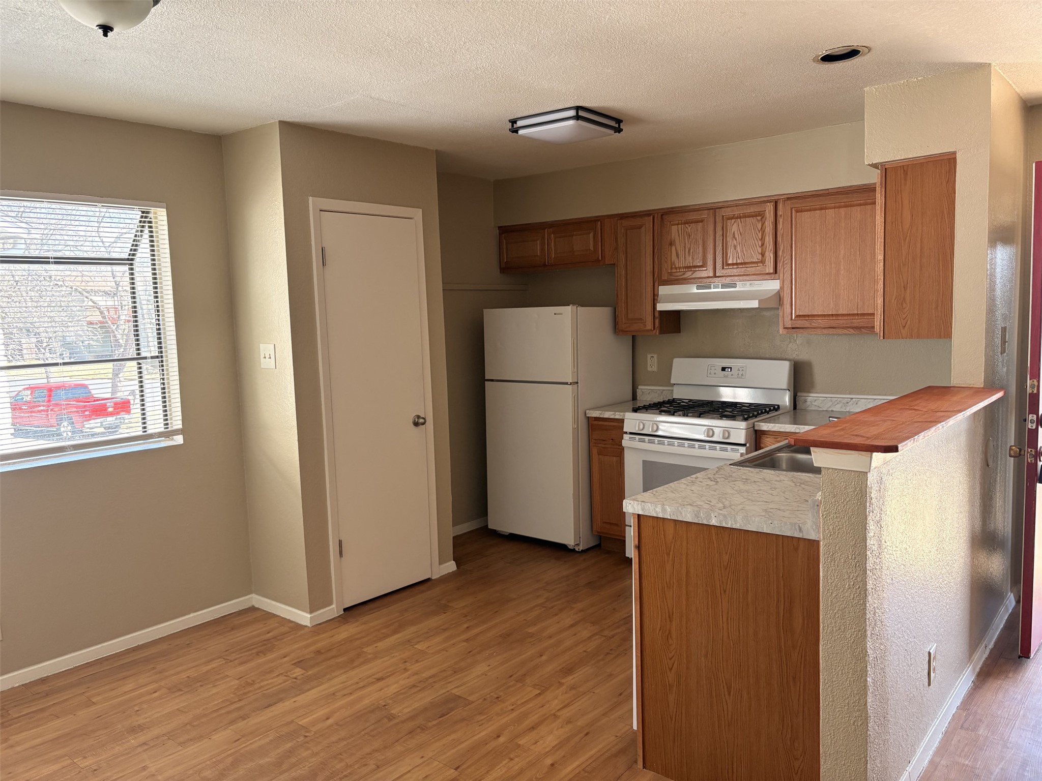 9902 Roxanna Drive, Unit D Austin, TX 78748 - Photo 1 of 19 Kitchen with white appliances, light wood finished floors, wood finish cabinetry, a textured ceiling, and a peninsula