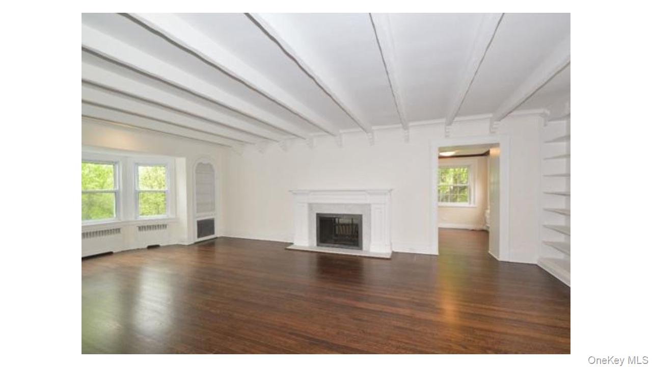 2 Arleigh Road Great Neck, NY 11021 - Photo 6 of 22 Exposed ceiling beams, rich wood-finish flooring, a classic fireplace with a stone surround, built-in shelving, and a bay window