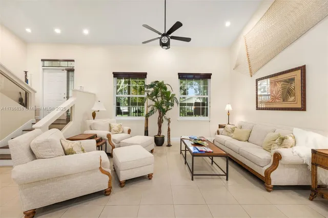 a living room with furniture a two large window and a ceiling fan
