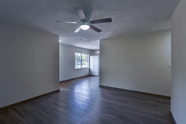 an empty room with wooden floor fan and windows