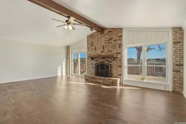 a view of an empty room and kitchen view with wooden floor