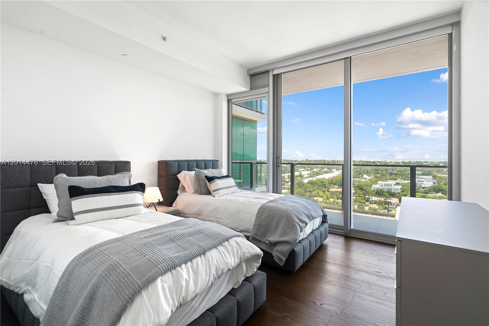 360 Ocean Drive, Unit 1106S Key Biscayne, FL 33149 - Photo 19 of 67 Bedroom with Balcony Access – A second bedroom features floor-to-ceiling glass doors, warm wood flooring, and direct balcony access with sweeping treetop and water views. Soft bedding and neutral tones enhance the calm, coastal feel.