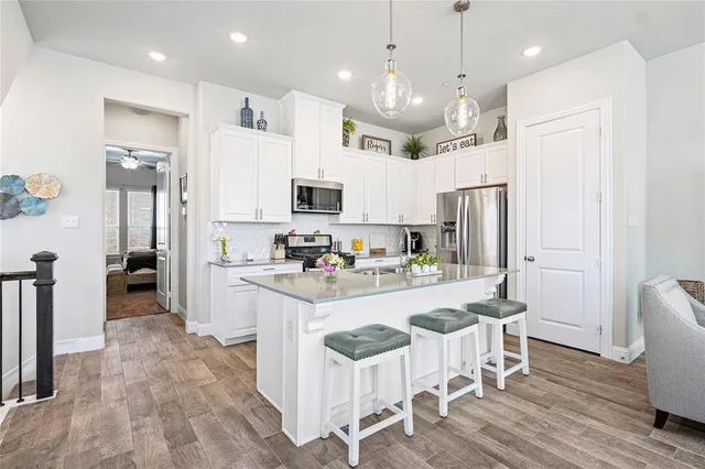 a kitchen with stainless steel appliances kitchen island granite countertop a refrigerator a stove top oven a sink dishwasher and white cabinets with wooden floor