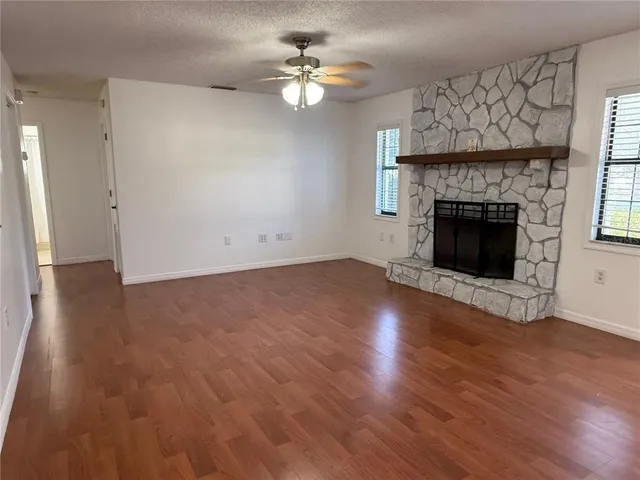 an empty room with wooden floor a fireplace a ceiling fan and windows