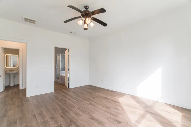 an empty room with wooden floor chandelier fan and windows
