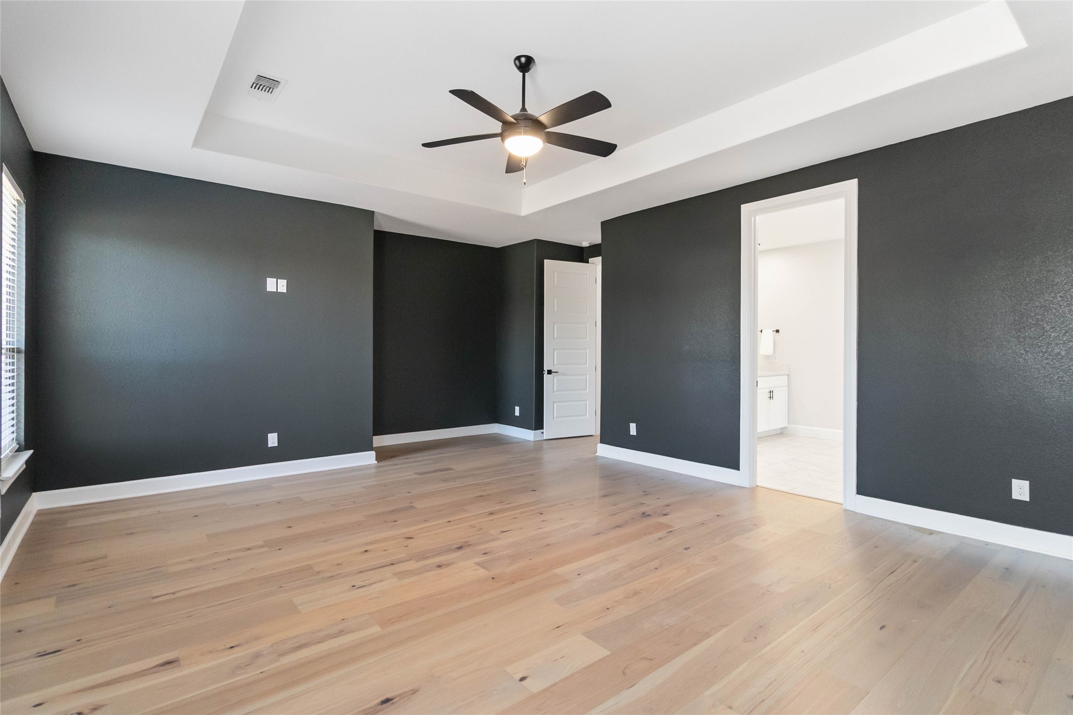 640 Prairie Clover Drive Dripping Springs, TX 78620 - Photo 14 of 32 Unfurnished bedroom featuring a tray ceiling, ceiling fan, light wood-style flooring, and ensuite bathroom