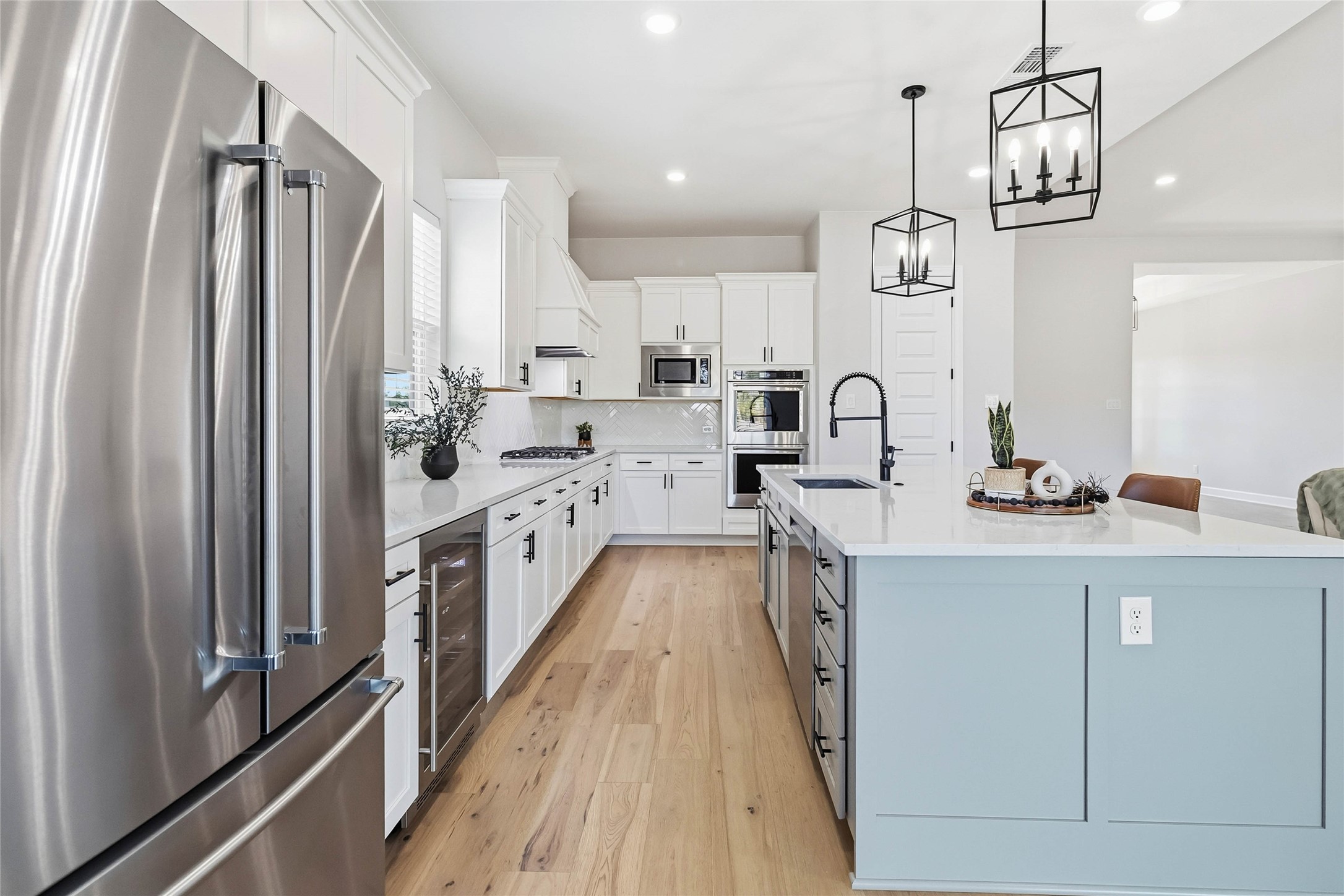 640 Prairie Clover Drive Dripping Springs, TX 78620 - Photo 10 of 32 Kitchen with appliances with stainless steel finishes, white cabinetry, light wood-type flooring, pendant lighting, and decorative backsplash