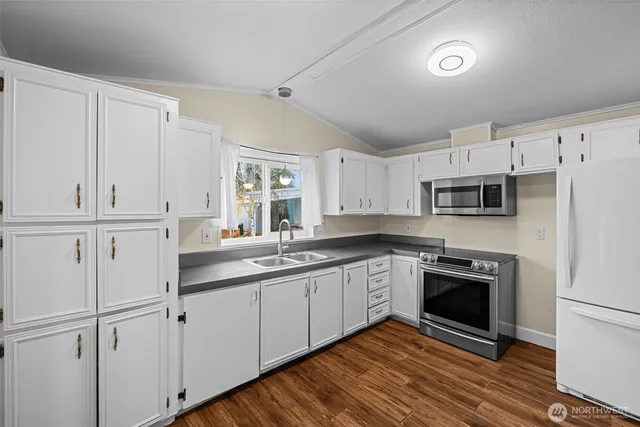 a kitchen with stainless steel appliances granite countertop a sink a stove a refrigerator and white cabinets