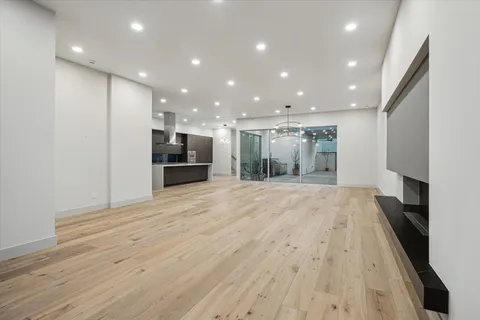 a view of an empty room with wooden floor and a kitchen