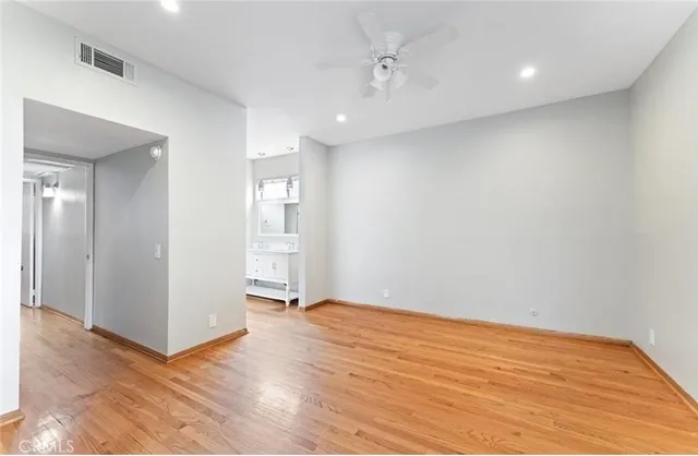 a view of an empty room with wooden floor and a kitchen