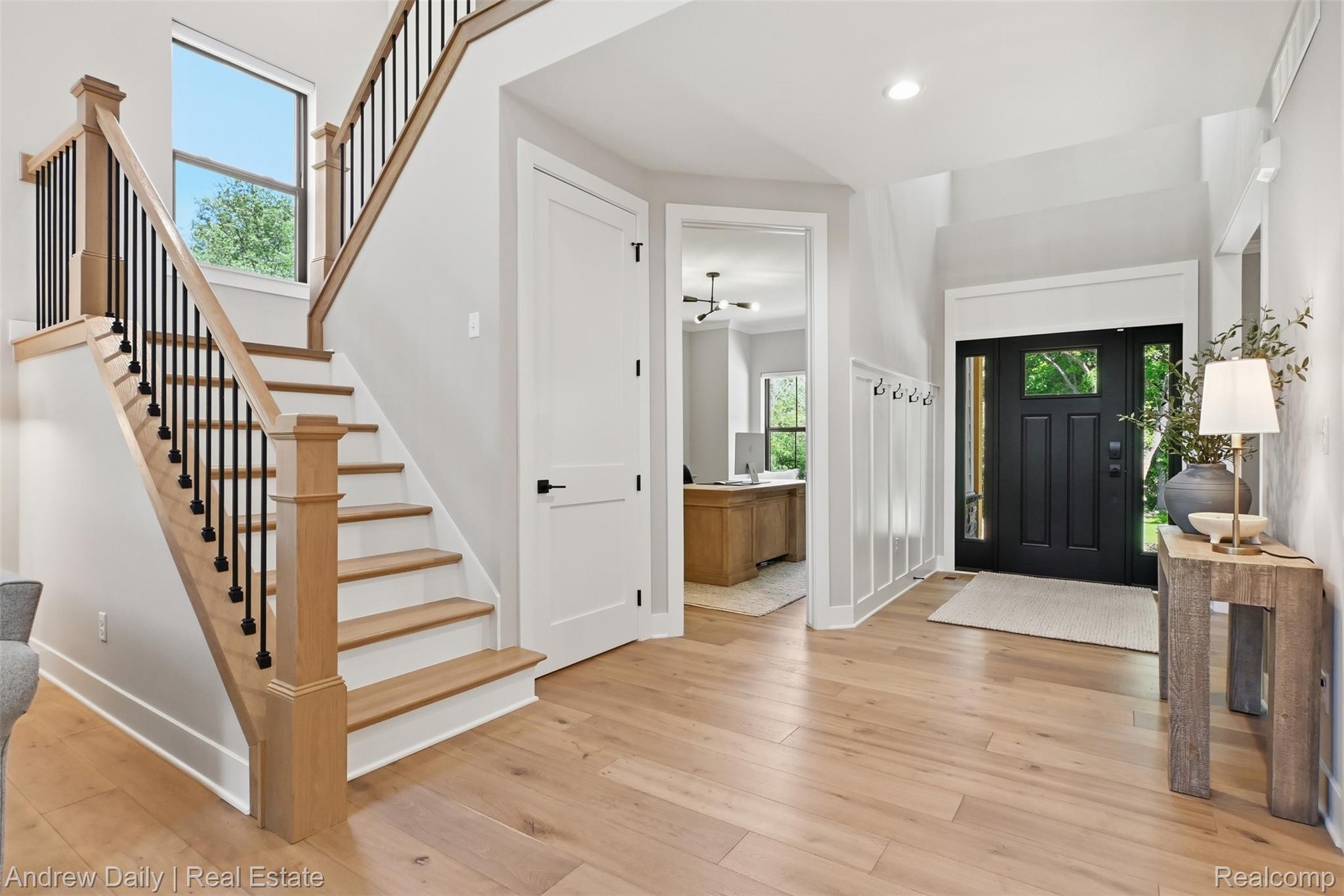4661 Spears Road Pinckney, MI 48169 - Photo 8 of 56 Bright entryway featuring light wood-finish flooring, a dark paneled entry door with sidelights, a wood and black metal staircase, and wainscoting with coat hooks