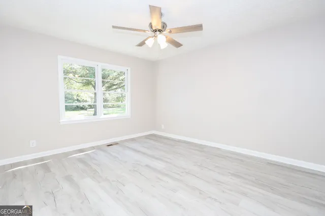an empty room with wooden floor chandelier fan and windows
