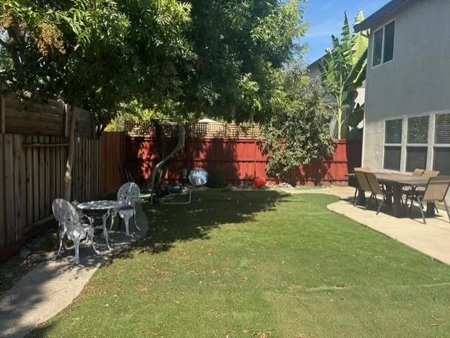 a view of a patio with table and chairs with wooden fence and large trees