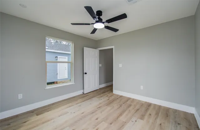 an empty room with wooden floor ceiling fan and windows