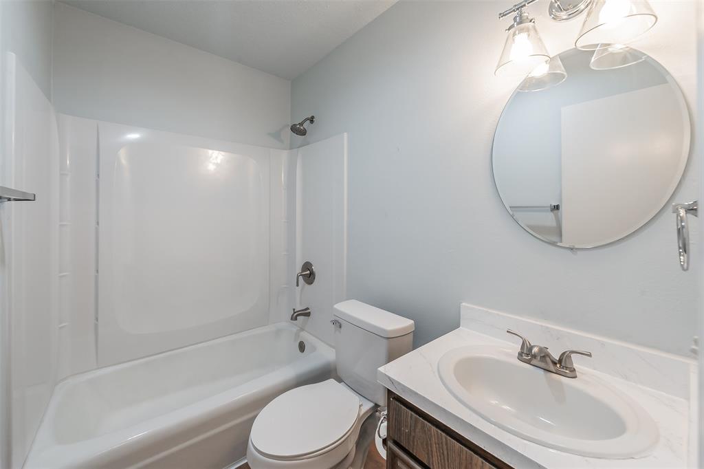 1301 Cedar Ridge Terrace Euless, TX 76039 - Photo 24 of 31 Bathroom featuring a combination bathtub and shower with a white surround, a round mirror, and a wood-finish vanity with a white countertop and oval sink