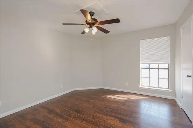 an empty room with wooden floor fan and windows