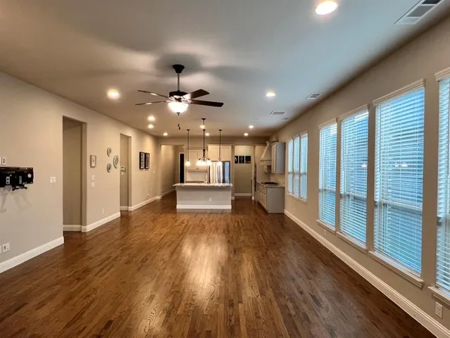 a view of an empty room with wooden floor and a kitchen