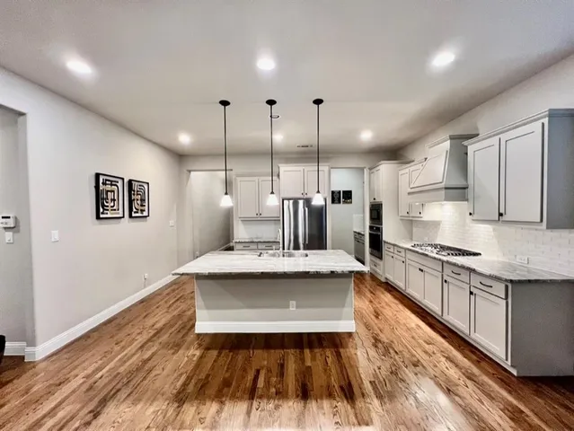 a large white kitchen with a stove a sink a chimney wooden floor and cabinets