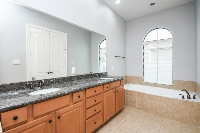 a spacious bathroom with a granite countertop sink a mirror and a bathtub