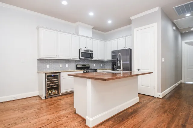 a kitchen with stainless steel appliances a microwave a stove a sink dishwasher a refrigerator and white cabinets with wooden floor