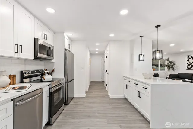 a kitchen with stainless steel appliances granite countertop a stove top oven a sink a refrigerator and white cabinets with wooden floor