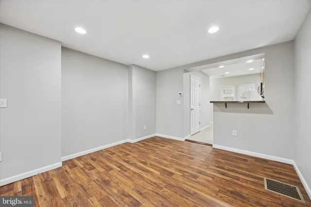 a view of empty room with wooden floor and kitchen