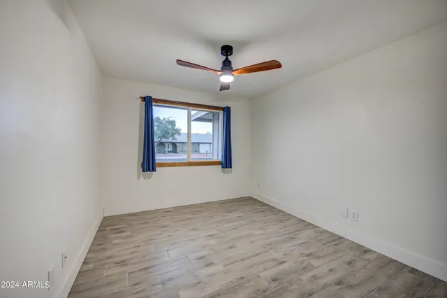 an empty room with wooden floor ceiling fan and windows