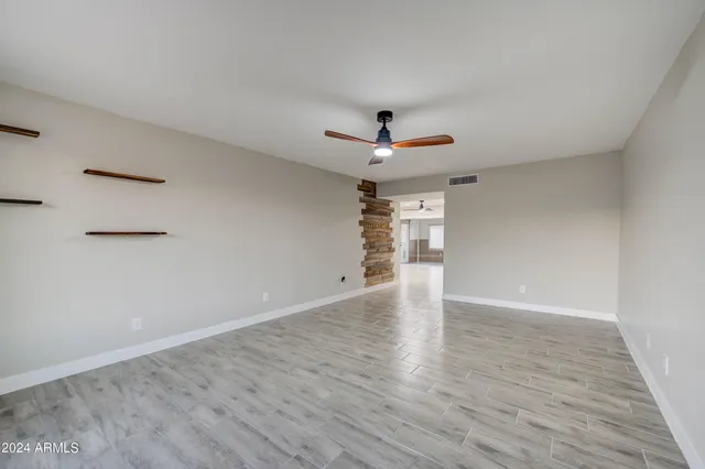 a view of an empty room with wooden floor and a ceiling fan