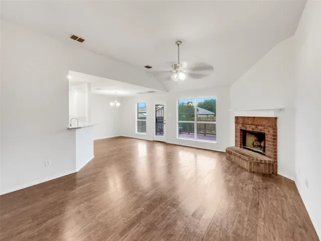an empty room with wooden floor fireplace and windows
