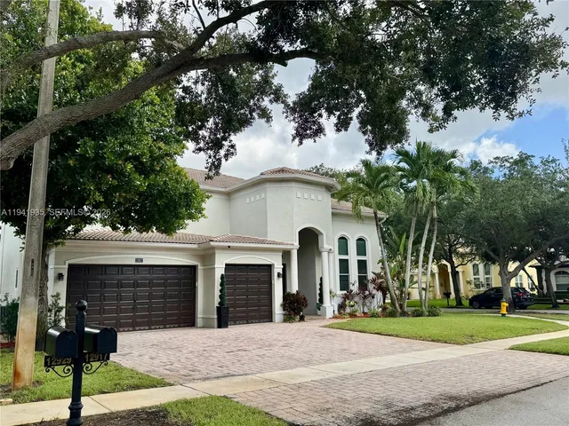 a view of a white house with a big yard and potted plants and a large tree