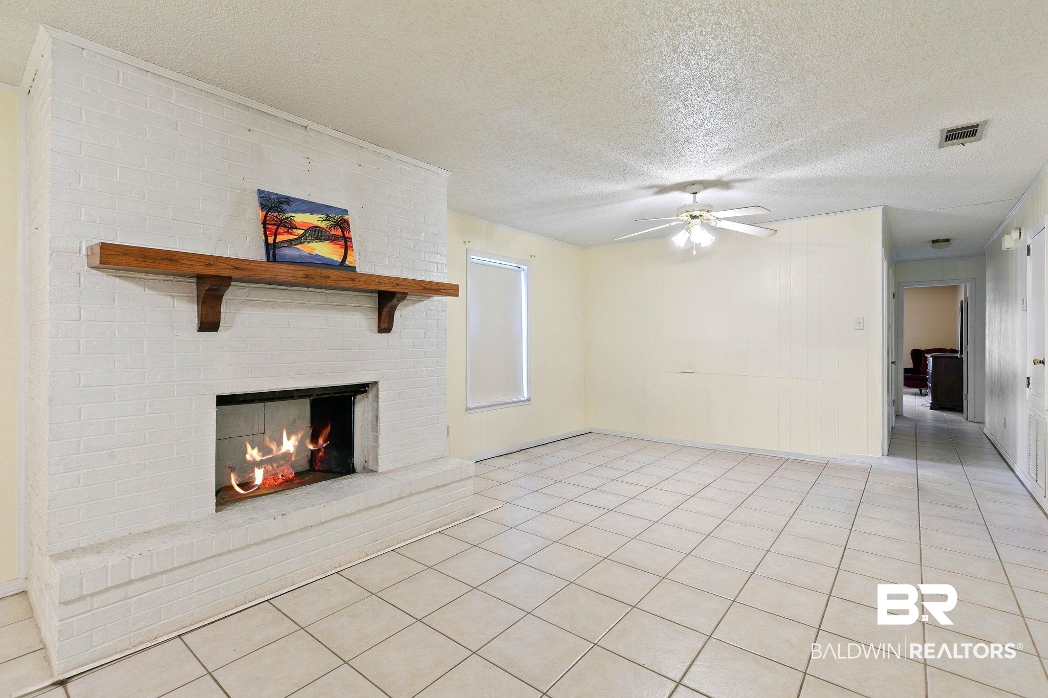 13653 Roberts Road Loxley, AL 36551 - Photo 9 of 33 Living area featuring a painted brick fireplace with a wood mantel, light-toned tile flooring, a ceiling fan with integrated lighting, and neutral wall tones