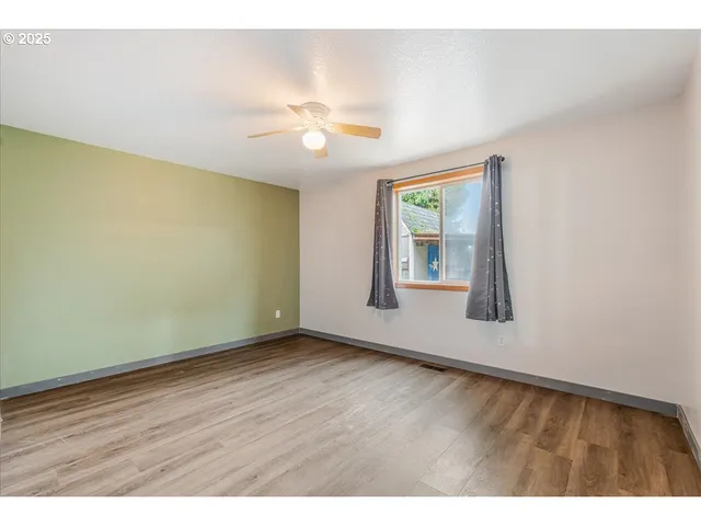 an empty room with wooden floor chandelier fan and windows