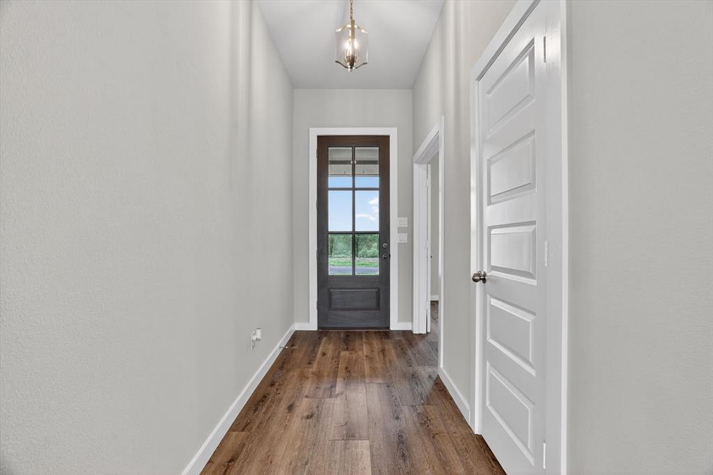 504 Clifton Court Springtown, TX 76082 - Photo 18 of 36 Entryway featuring wood-finish flooring, light gray walls, a dark paneled door with glass inserts, and a decorative pendant light fixture