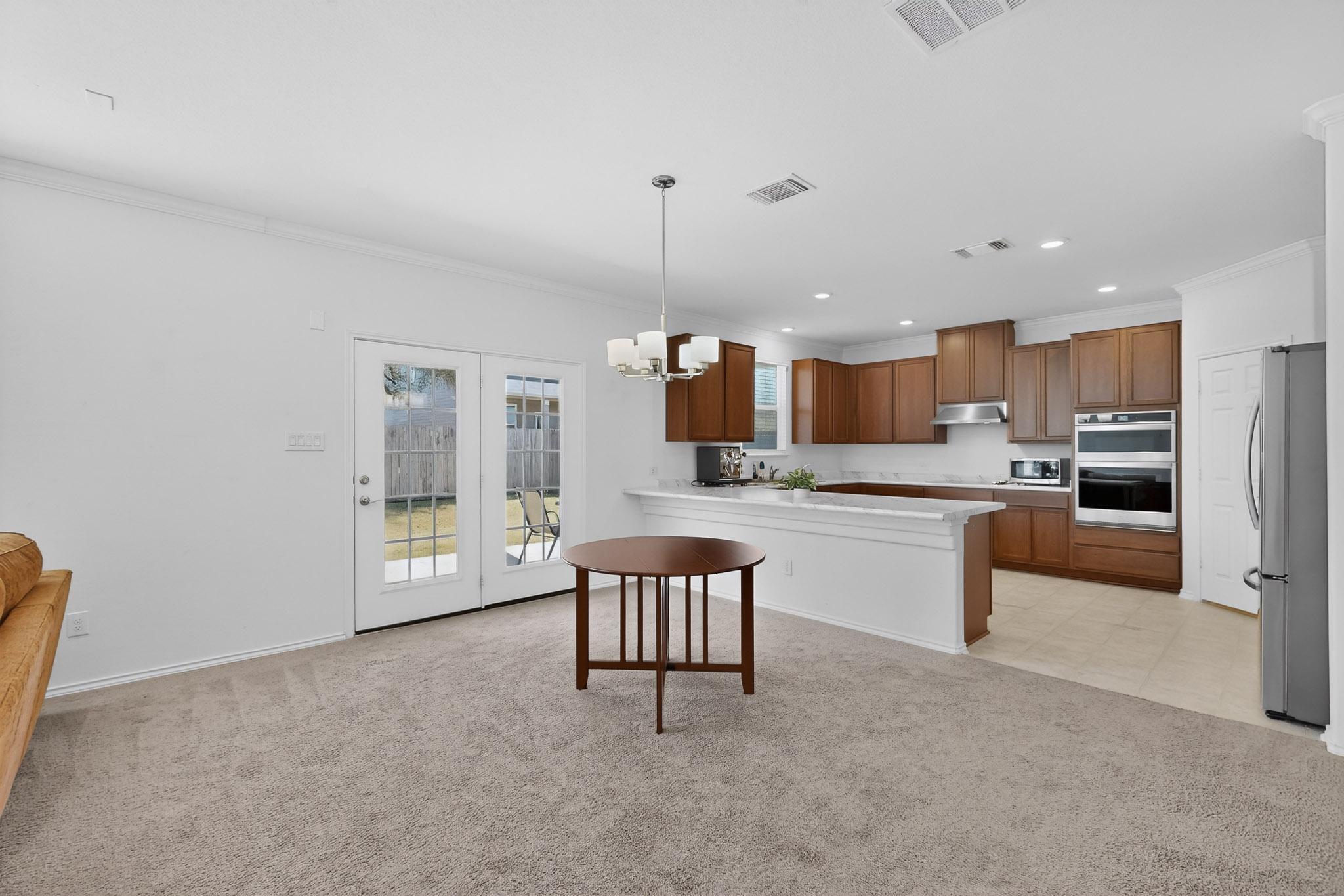 712 Madalin Rue Court Leander, TX 78641 - Photo 5 of 28 Kitchen featuring wood finish cabinets, a peninsula, ornamental molding, hanging lights, and light carpet