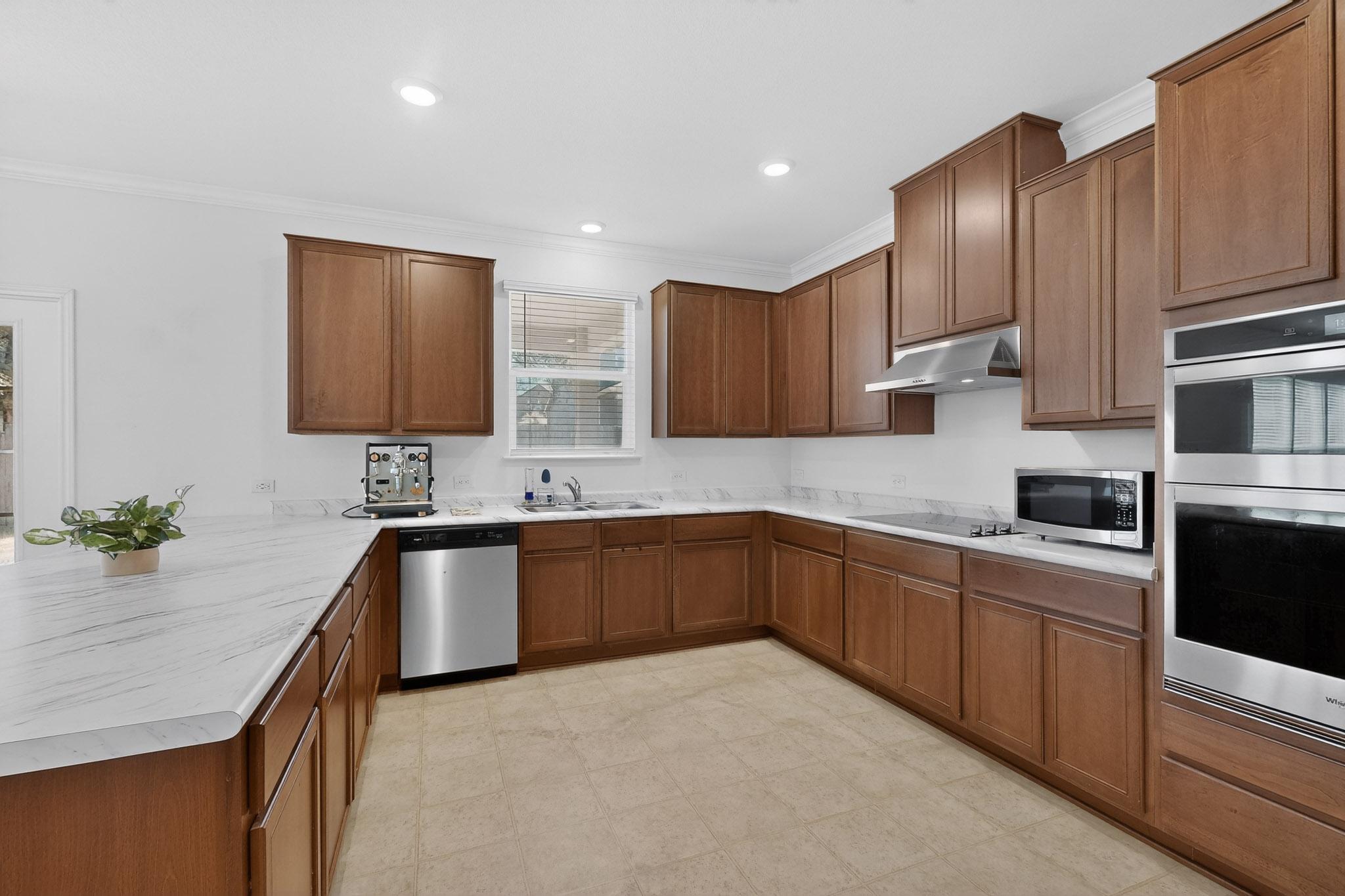 712 Madalin Rue Court Leander, TX 78641 - Photo 8 of 28 Kitchen with a peninsula, stainless steel appliances, ornamental molding, light countertops, and wood finish cabinets