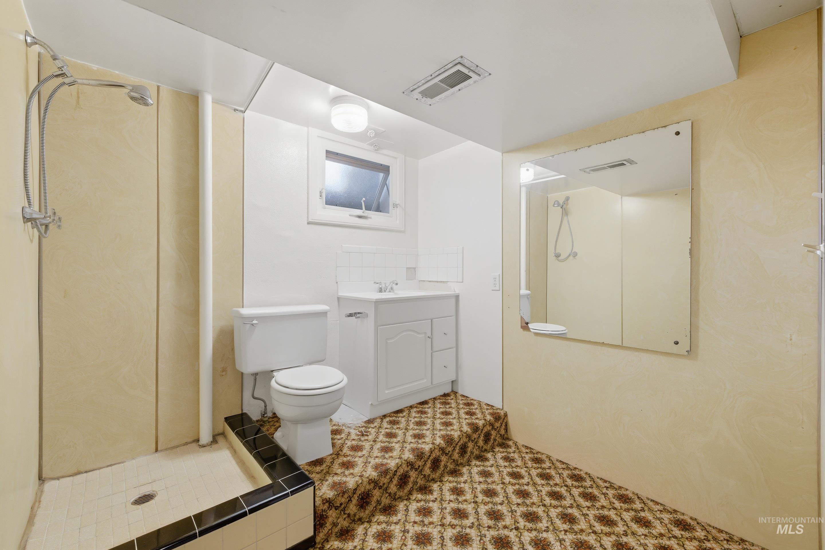 504 West Howe Street Boise, ID 83706 - Photo 35 of 47 Bathroom featuring a standing shower with a tiled base and dark trim, a white vanity with a single sink, a toilet, a window, and a wall-mounted mirror