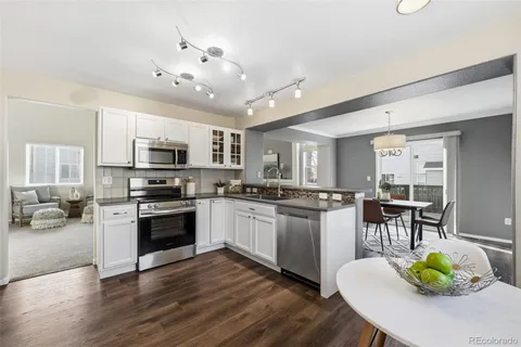 a kitchen with stainless steel appliances granite countertop a stove top oven a sink dishwasher a dining table and chairs with wooden floor