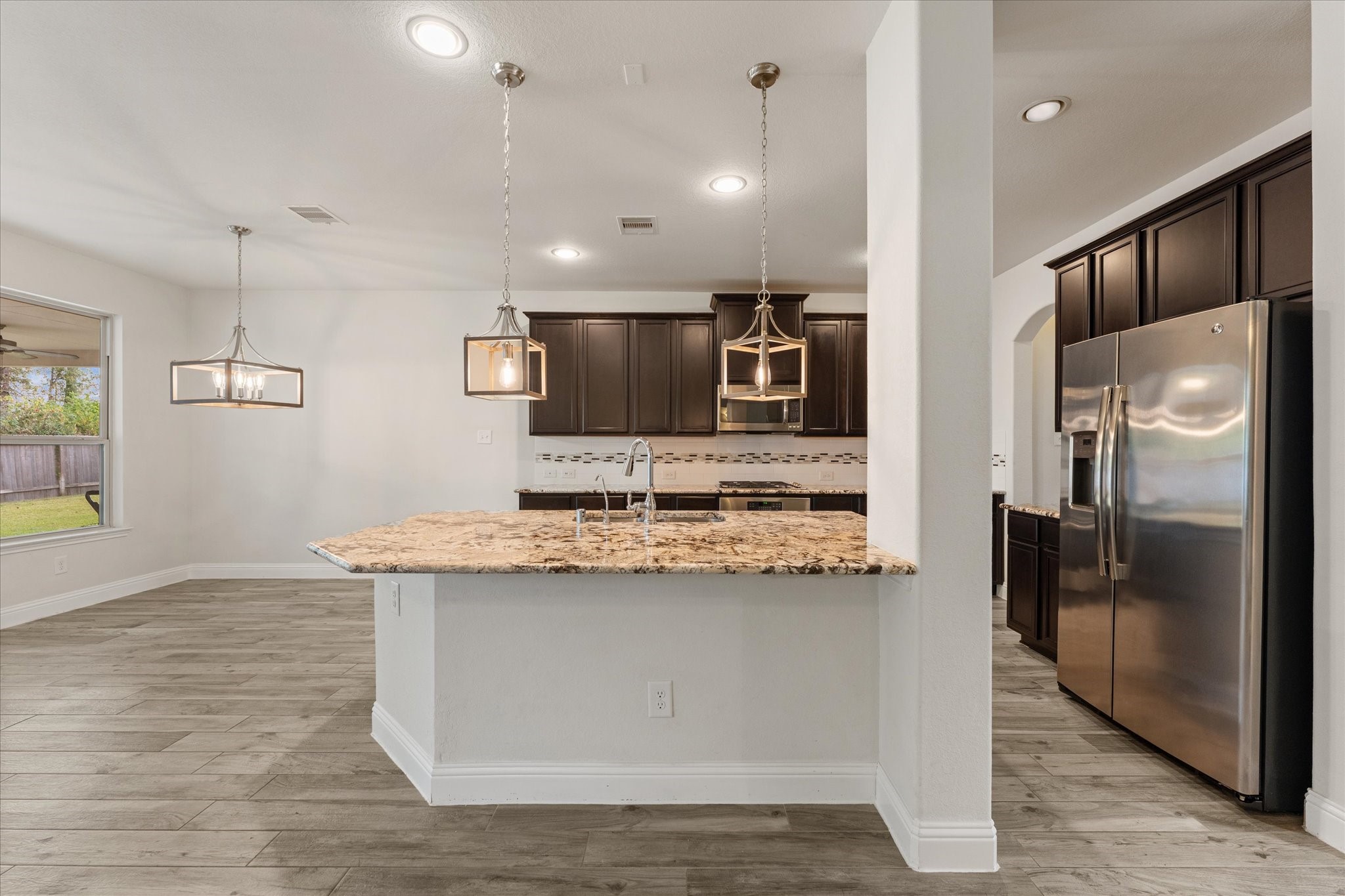 3402 Dryer Park Drive Spring, TX 77373 - Photo 12 of 40 This modern kitchen features dark cabinetry, stainless steel appliances, and a spacious granite countertop island with pendant lighting. The open layout flows into a bright dining area with large windows and stylish light fixtures, creating a welcoming space for entertaining.