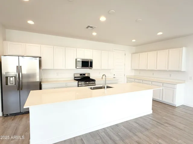 a large kitchen with stainless steel appliances a large counter top a stove a refrigerator a sink a center island and couches